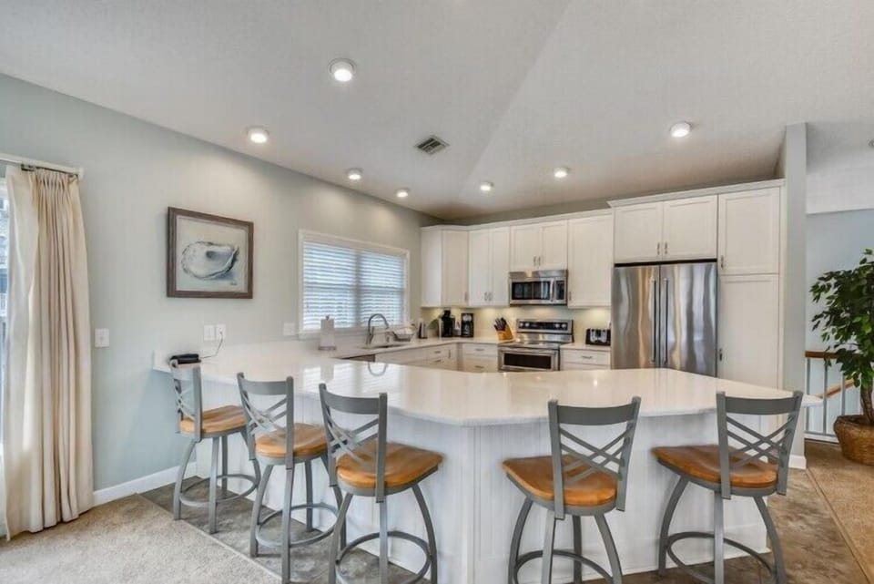 Your open-concept kitchen invites you to gather around the spacious island, where gleaming countertops and modern appliances make cooking a joy. Bright recessed lighting and soft coastal tones create a warm, welcoming space for your vacation memories.