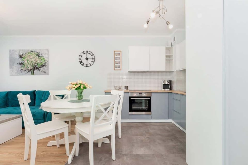 A bright living room space with a kitchenette that is connected by a table with a round top. 