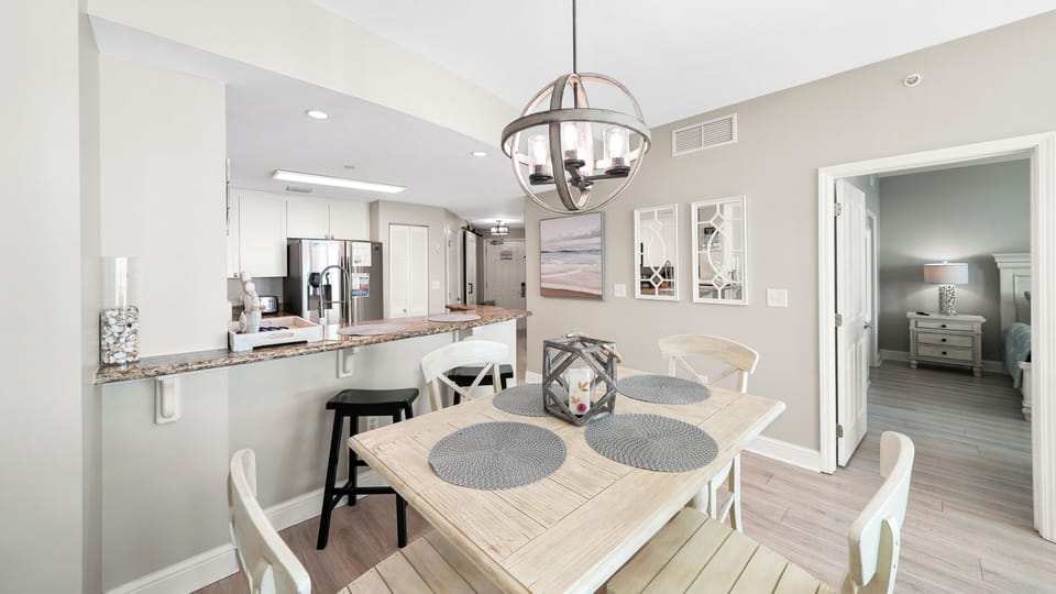 Savor your morning coffee in this bright, open dining area where modern design meets coastal comfort with stylish lighting and granite countertops.