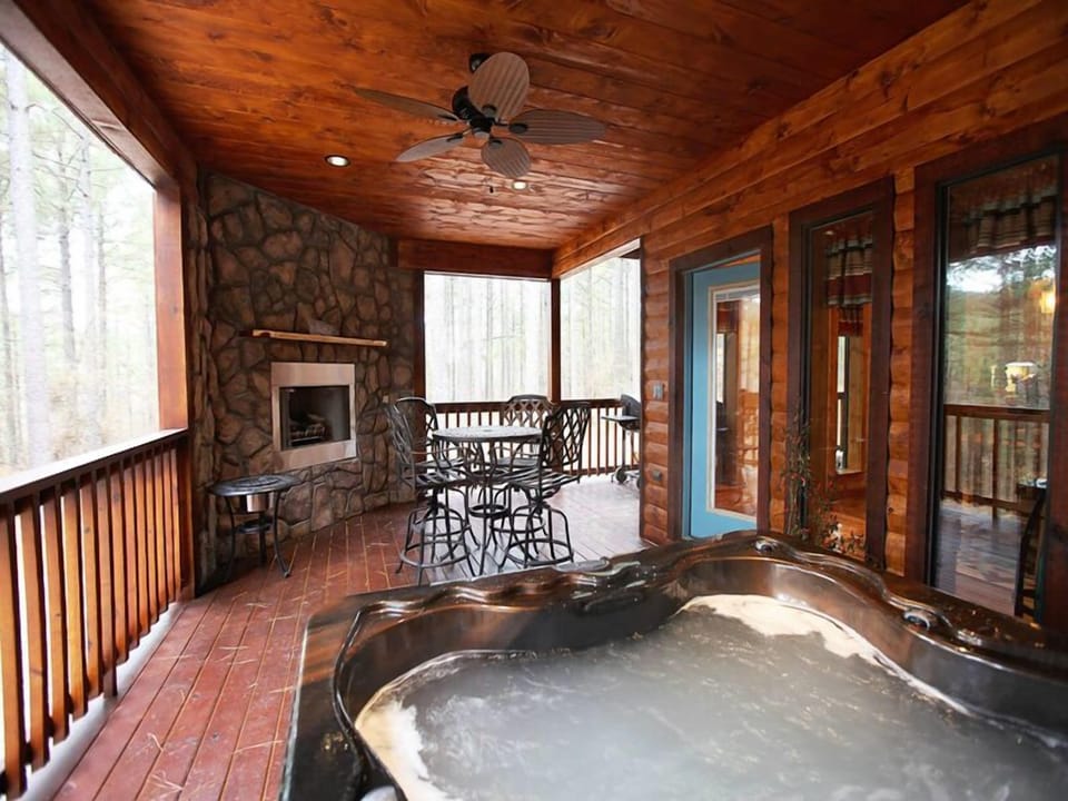 Relax in this covered outdoor retreat, featuring a bubbling hot tub, cozy fireplace, and inviting seating for year-round enjoyment.