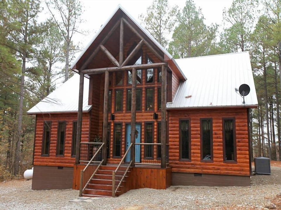 A stunning timber-framed cabin exterior showcases grand windows and rustic craftsmanship, blending beautifully with its natural surroundings.