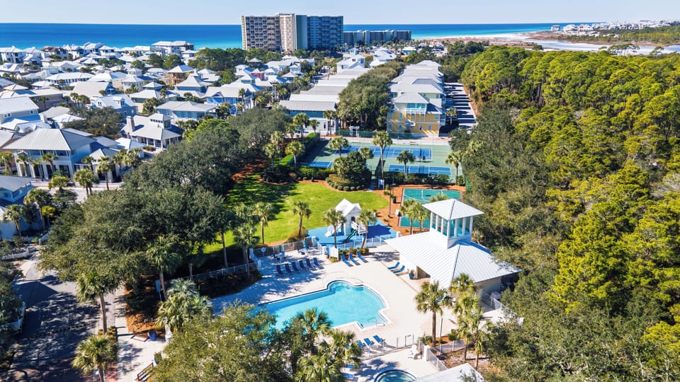 Aerial view of a resort community featuring pool facilities, recreational areas, and nearby beach access in a lush coastal setting.
