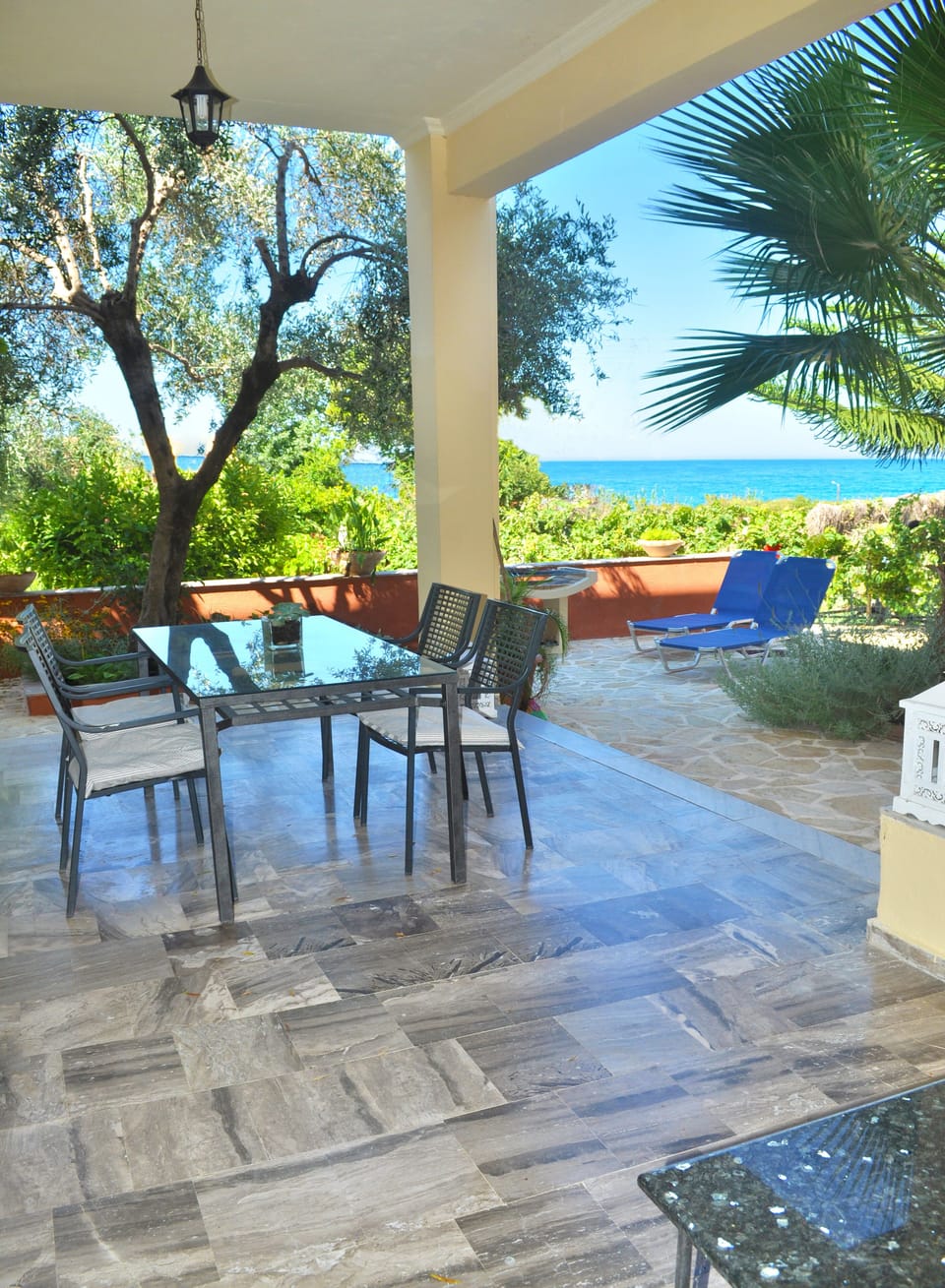 Large covered terrace with garden furniture and a view of the sea.