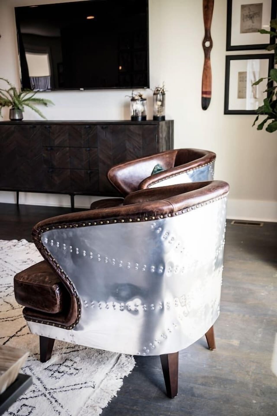 Sleek leather armchairs with metal rivet accents add vintage aviation inspired character - Polished metallic backrests & rich brown leather bring texture & style to the space - Positioned perfectly for conversation or TV viewing in the living area