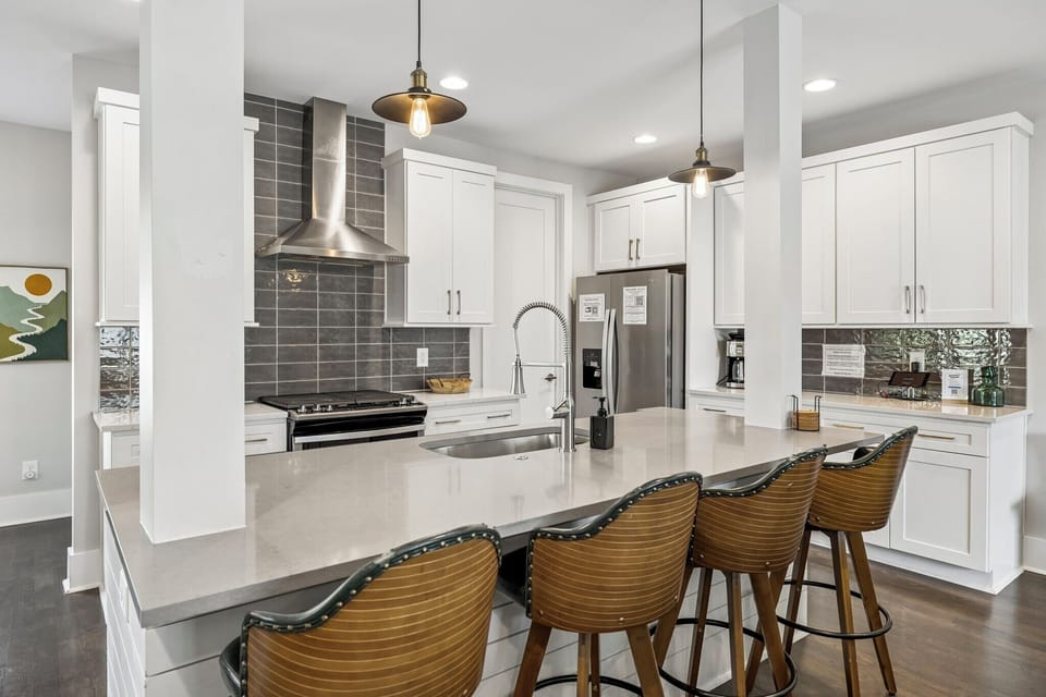 Kitchen with sleek white cabinetry, quartz counters, & stainless steel appliances - Spacious island with seating for four & pendant lighting ideal for gathering & dining - Subway tile backsplash & open layout create a modern, welcoming culinary space