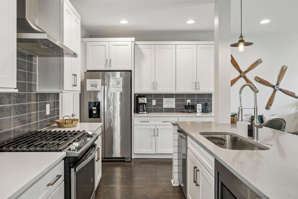 Full gourmet setup with stainless steel appliances, gas range, and large center island - Chic pendant lights, neutral tile backsplash, and extra counter space for easy prep - Wine and snack board welcome you into this stylish, functional culinary space