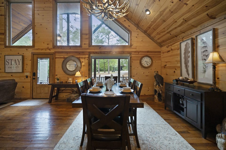Gather around the spacious dining table beneath a rustic chandelier, perfect for enjoying meals together in a warm cabin setting.