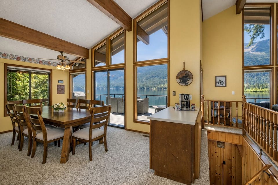 Your lakefront dining space features panoramic mountain views through floor-to-ceiling windows, with a kitchen island perfect for morning coffee.