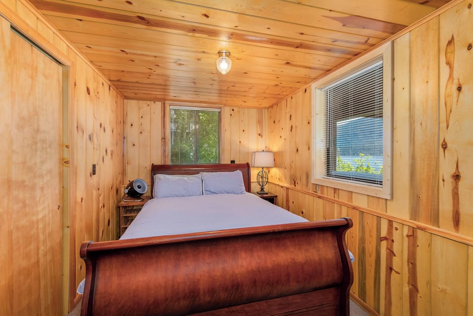 Queen bed nestled in a warm knotty‑pine bedroom with gentle natural light