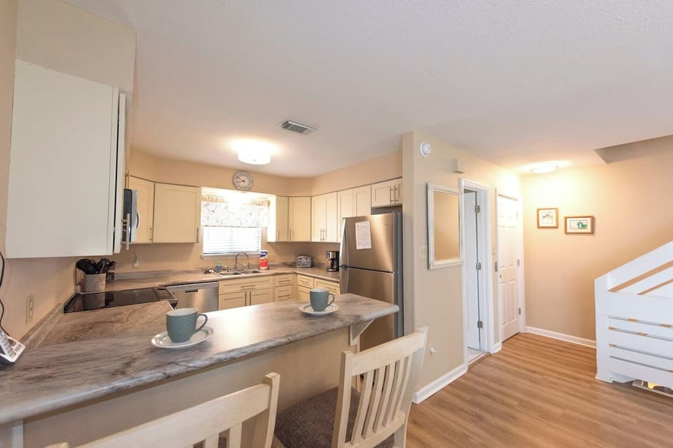 Cook a full vacation meal without leaving anything behind — the kitchen has a proper breakfast bar, white cabinets stocked with what you need, and three barstools for whoever wanders in first.