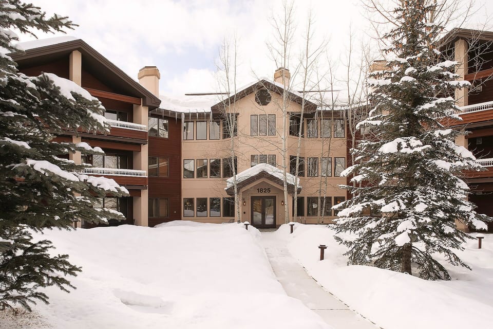 Snow-covered mountain resort property with multiple buildings nestled among evergreen trees, creating a perfect winter wonderland setting.