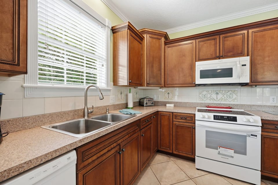 Cook up your vacation favorites in this fully equipped kitchen with rich cabinetry, modern appliances, and plenty of counter space for meal prep. Natural light streams through the window, making your cooking experience bright and enjoyable.