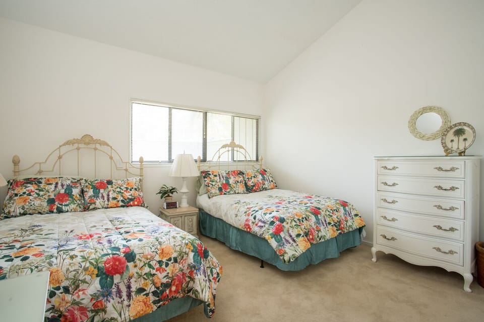 - Cheerful bedroom features two full beds with bright floral bedding and vintage flair
- Plenty of room for guests, kids, or couples to spread out and rest in style
- Dresser, side table, and soft lighting complete this charming retreat