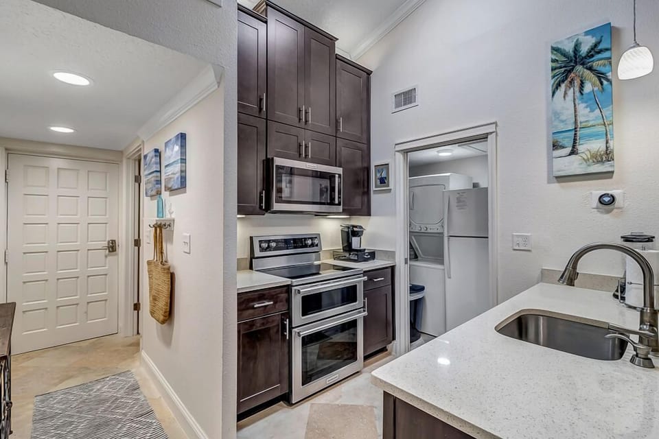- Compact yet stylish kitchen with stainless steel appliances and quartz counters
- Dark wood cabinetry offers contrast and plenty of storage space for essentials
- Convenient layout with open access to laundry and view into main living space