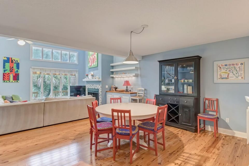 - Vibrant dining space with seating for six around a round white dining table
- Colorful red chairs add a playful pop against cool blue walls and wood floors
- Charming hutch stores dinnerware and adds rustic elegance to every meal