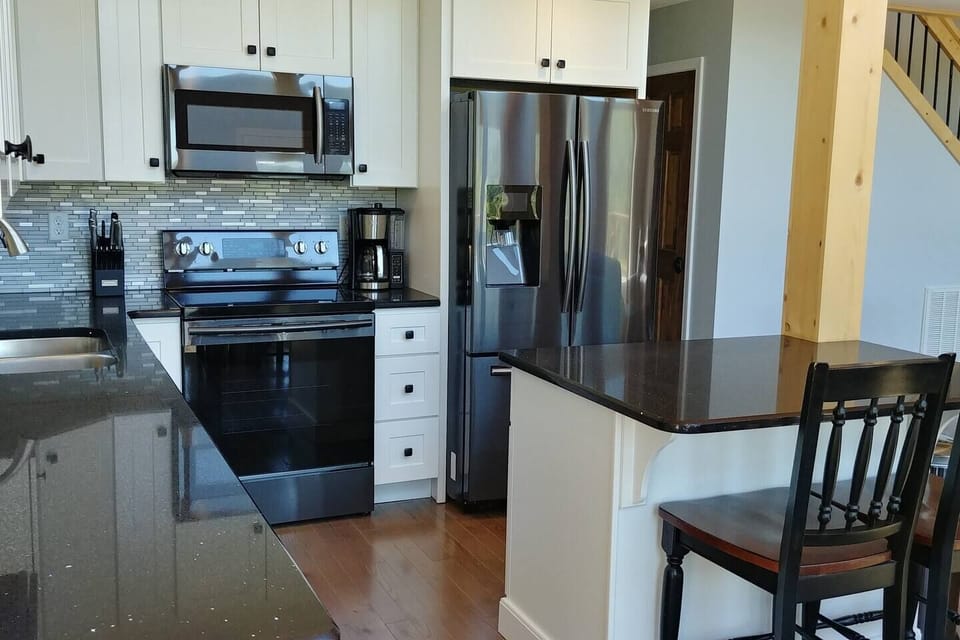 Modern full-size kitchen equipped with everything you may need, featuring granite countertops and a small island with barstool seating — perfect for cooking, dining, and gathering.