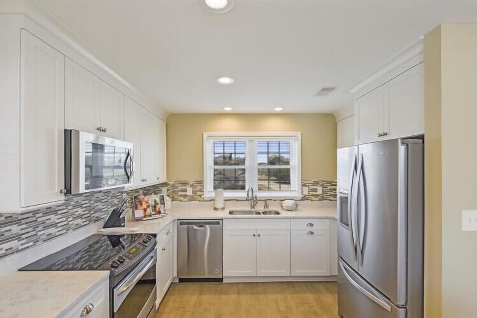 Your fully-equipped kitchen features sleek stainless steel appliances, ample counter space for meal prep, and modern cabinetry. Natural light pours through the window above the sink, creating a bright and welcoming space for cooking.