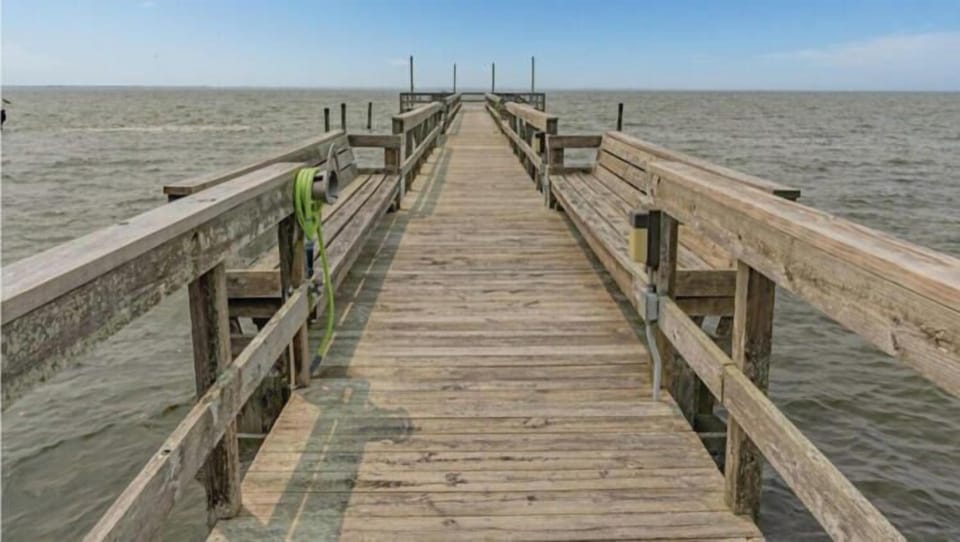 The Ships Watch Community Sound Pier stretches over calm coastal waters, offering serene views and direct access to waterfront activities in this peaceful seaside neighborhood.