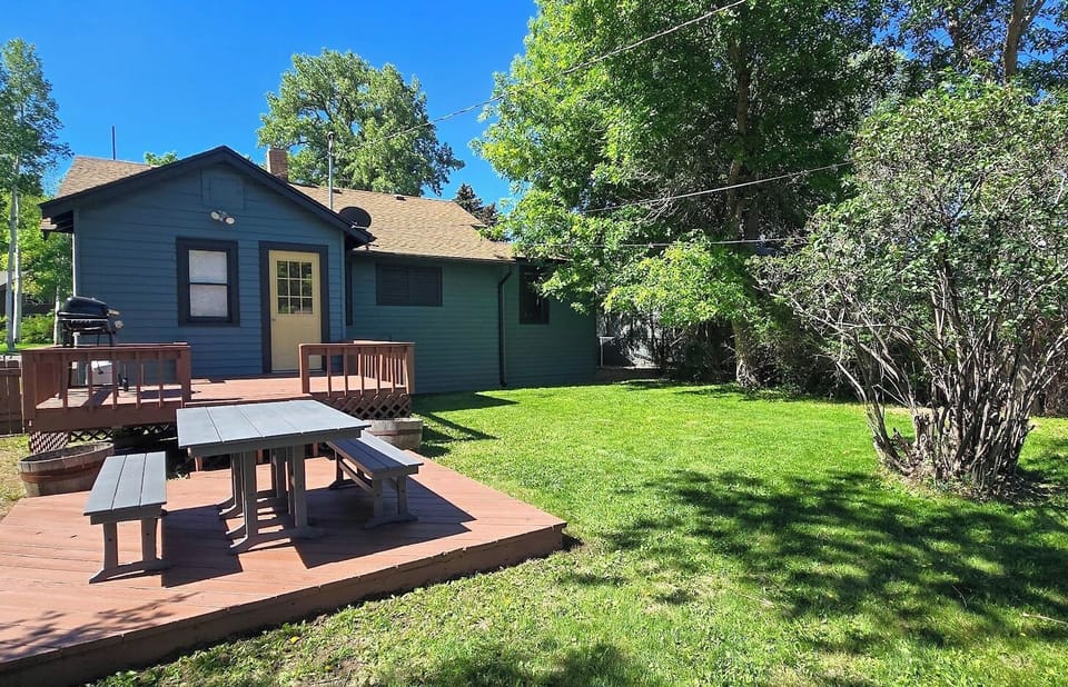 Large backyard feels like an oasis with a deck, outdoor dining space and gas grill