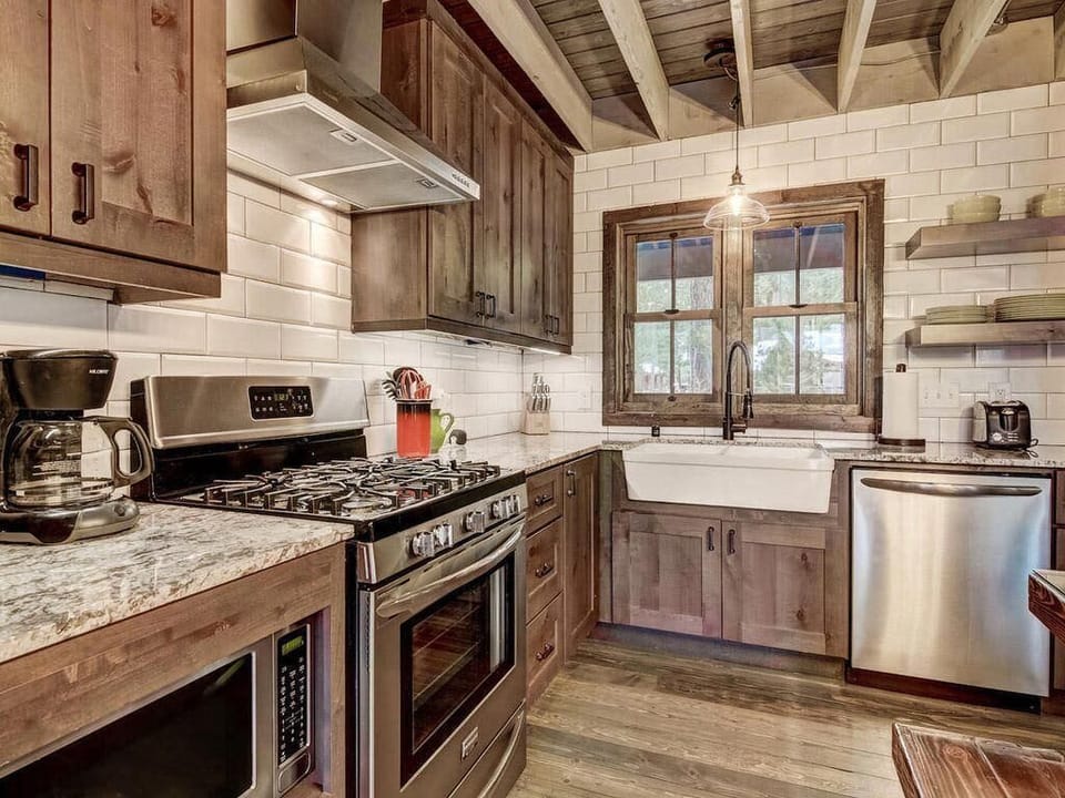 Rustic kitchen with wood cabinets, farmhouse sink beneath a wood-framed window, and stainless steel appliances.