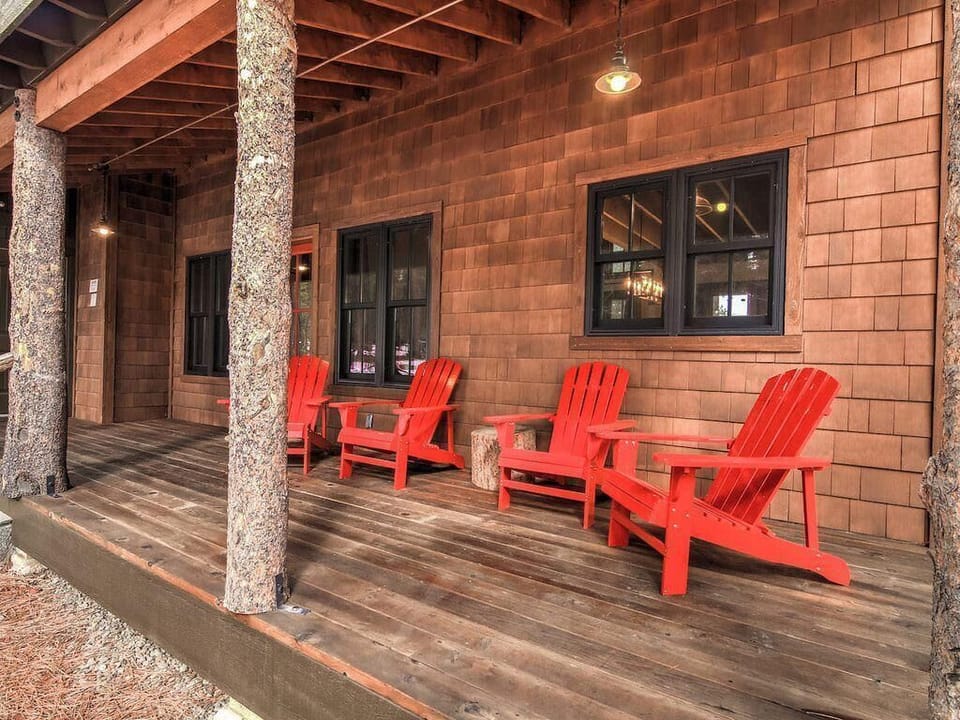 Covered back porch with tree-trunk columns, weathered wood decking, and four bright red Adirondack chairs.