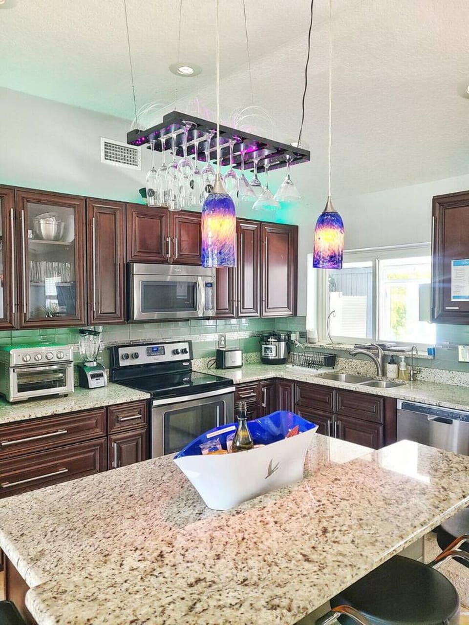 Gourmet kitchen with dark wood cabinets, colorful blue pendant chandelier, green tile backsplash and stainless steel appliances, Orlando