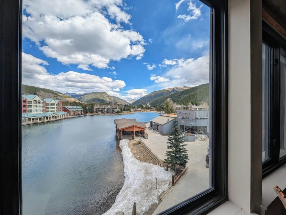 Stunning lakefront view framed by snow-capped mountains and resort buildings from this bright window.