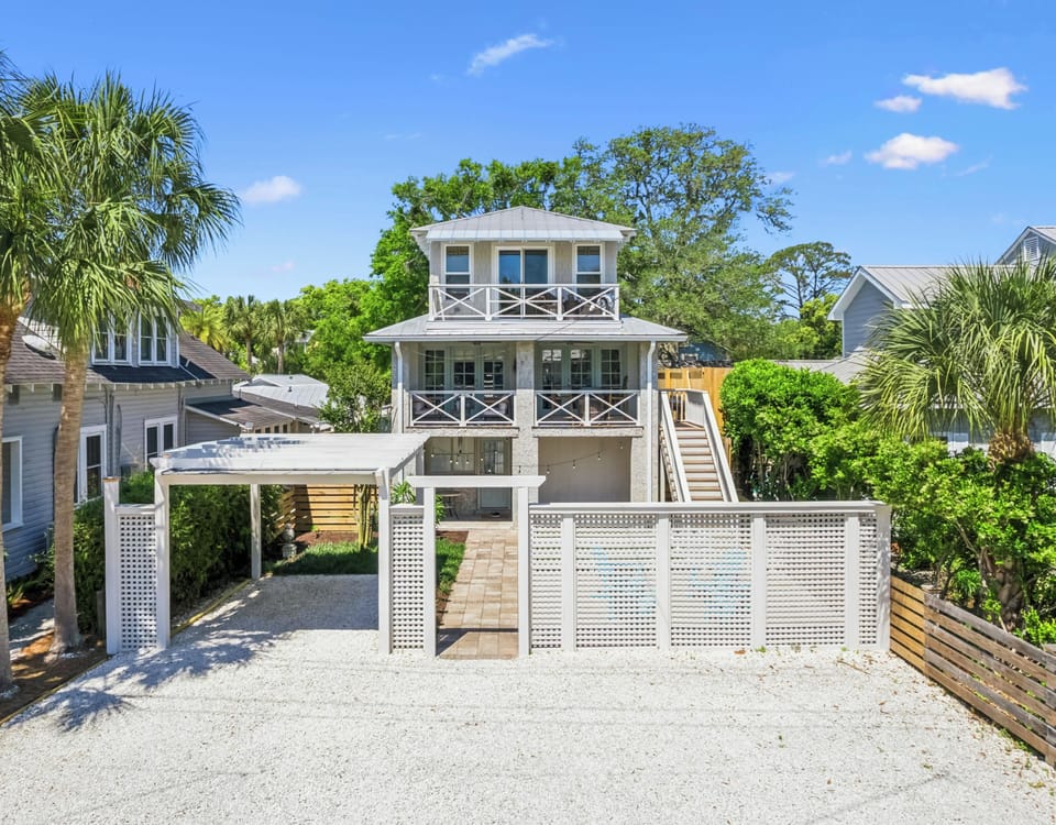Parking in front of the home. Charming coastal home with elegant white railings and tropical landscaping, nestled in a peaceful neighborhood setting.