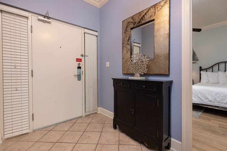 Step into a welcoming entryway featuring stylish decor, a sleek mirror, and a glimpse of the cozy bedroom beyond