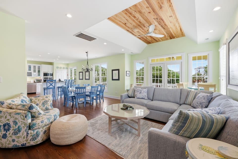 Relax in your bright, open living space featuring vaulted ceilings with warm wood accents, plush seating, and cheerful coastal decor—perfect for gathering with family or unwinding after a beach day.