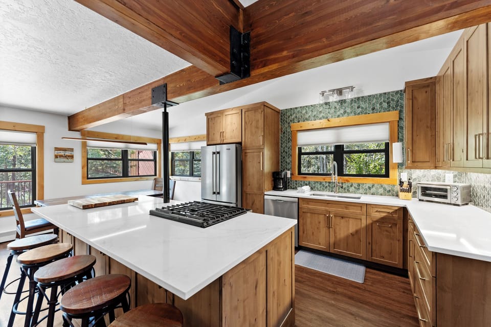 Cook in your dream kitchen with rich wood beams, spacious island, and modern appliances surrounded by forest views.