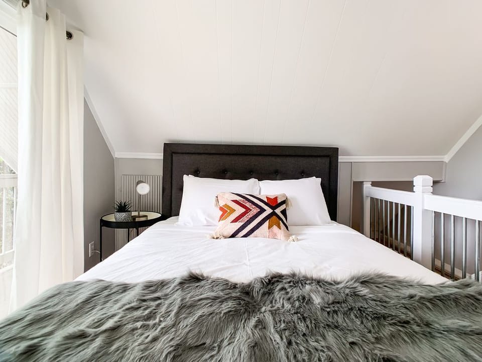 Bright and airy upstairs bedroom featuring a cozy queen size bed, Smart TV and access to the balcony to relax on after a long day.