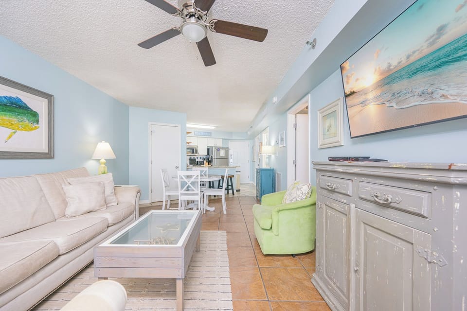 Living space featuring a cozy sofa, vibrant green chair, and a large TV showcasing a beach scene