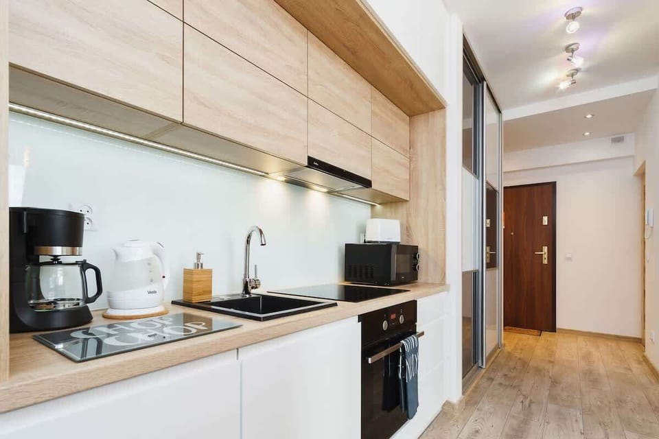 A sleek, modern kitchen with wood accents and white cabinetry. It’s small but functional, with essential appliances.