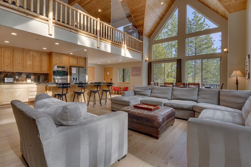 - Spacious open living room with vaulted ceilings and tall windows  
- Cozy seating with modern kitchen and dining area for gatherings  
- Natural wood accents bring warmth to the mountain retreat