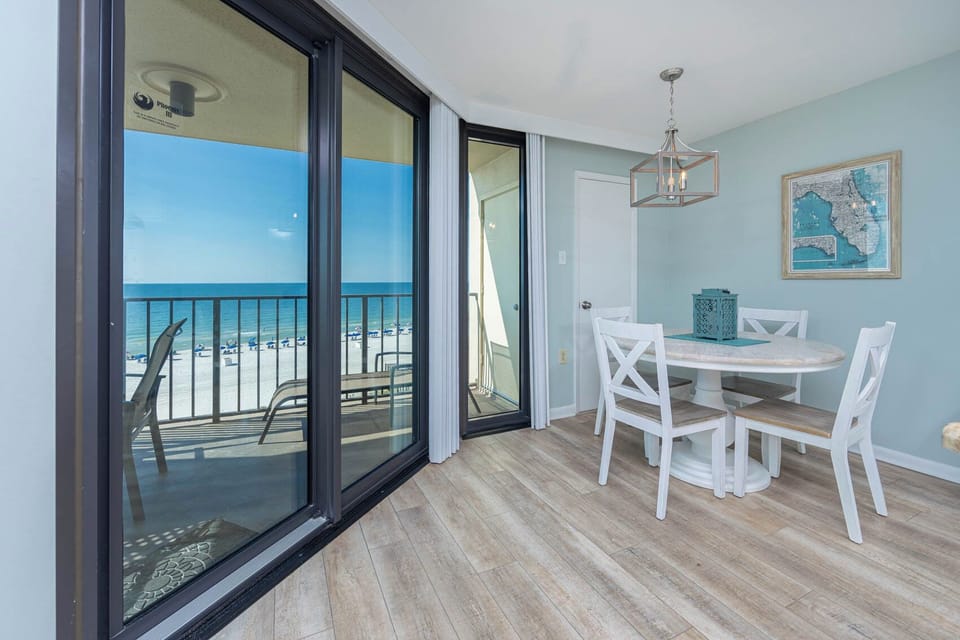 Bright dining area featuring a round table with white chairs and a view of the beach through large sliding glass doors