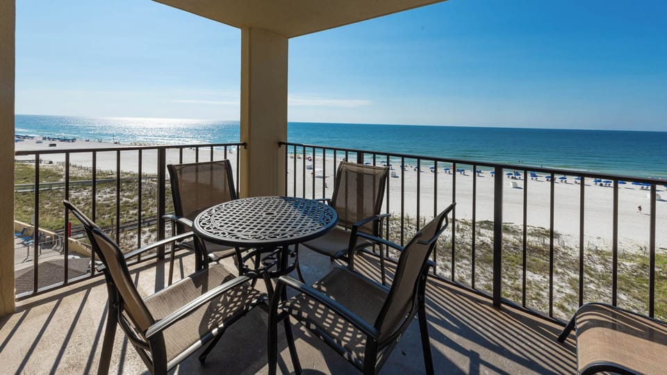 The balcony features a round table and chairs, offering a direct view of the beach and glistening water beyond