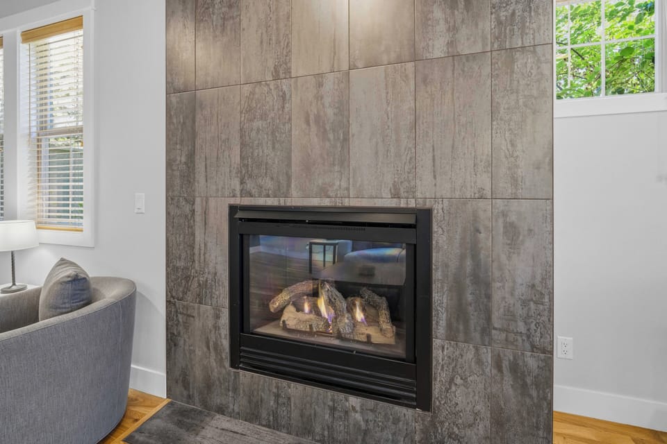 Cozy up beside your private fireplace, surrounded by elegant wood-textured tiling and natural light streaming through bright windows—your ideal retreat after a day of adventures.