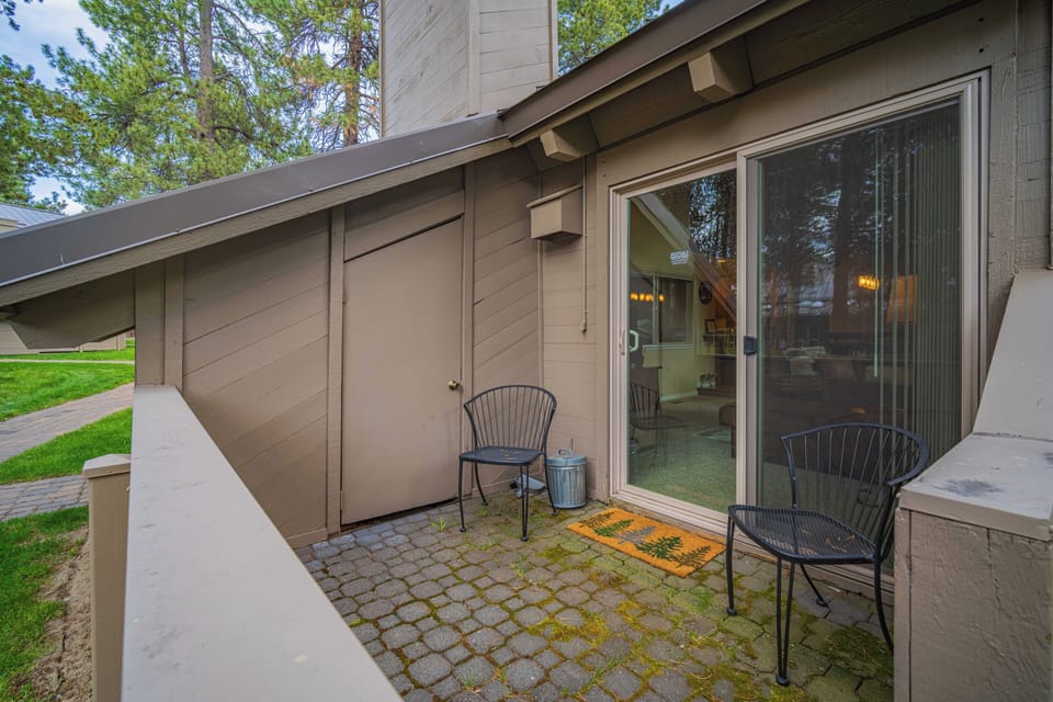 Charming private entrance with patio seating nestled among tall pines. Step inside through sliding glass doors to discover your cozy retreat, where warm lighting welcomes you home after exploring.
