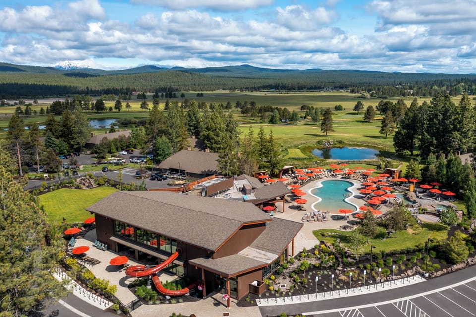 Aerial view of the property showcasing its expansive resort-style grounds, pool area, outdoor dining spaces, and scenic surroundings with mountain views and golf course.