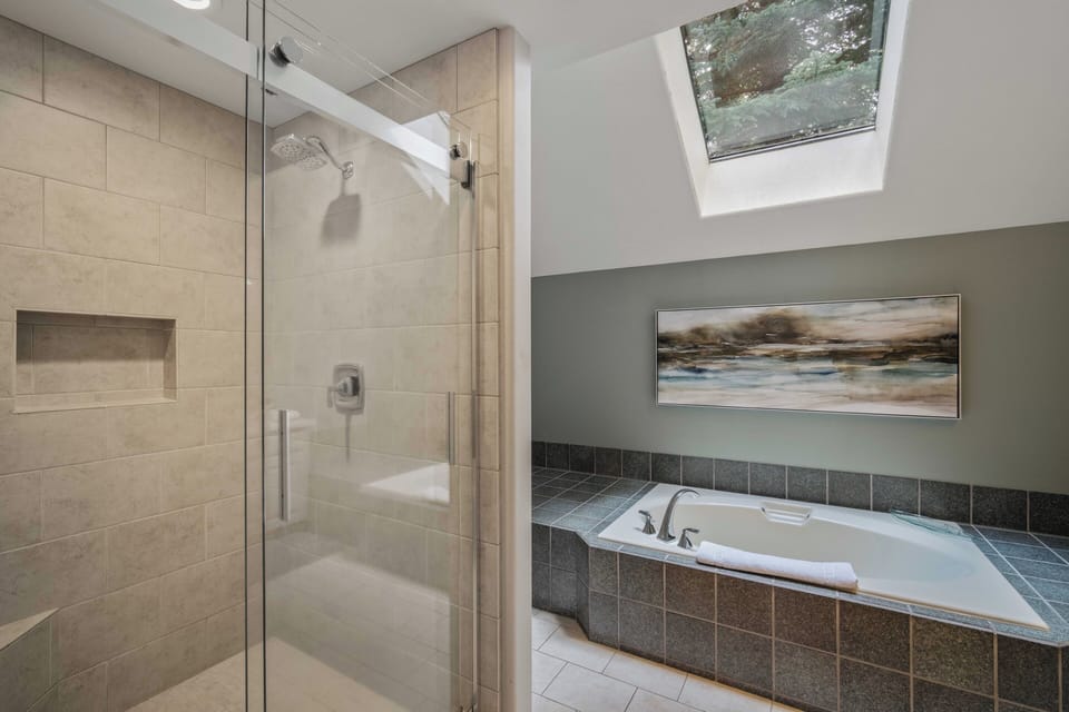Unwind in your spa-like bathroom featuring a luxurious jetted tub and glass-enclosed shower, all bathed in natural light from the skylight above.