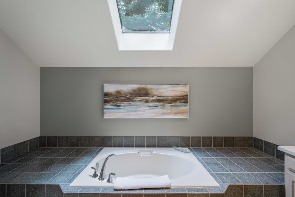 Unwind in your private spa-like bathroom with a deep soaking tub beneath a skylight, where natural light creates the perfect atmosphere for relaxation.