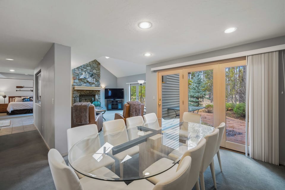 Your elegant dining space features a stunning glass table surrounded by plush white chairs, with natural light streaming through French doors to the peaceful patio.