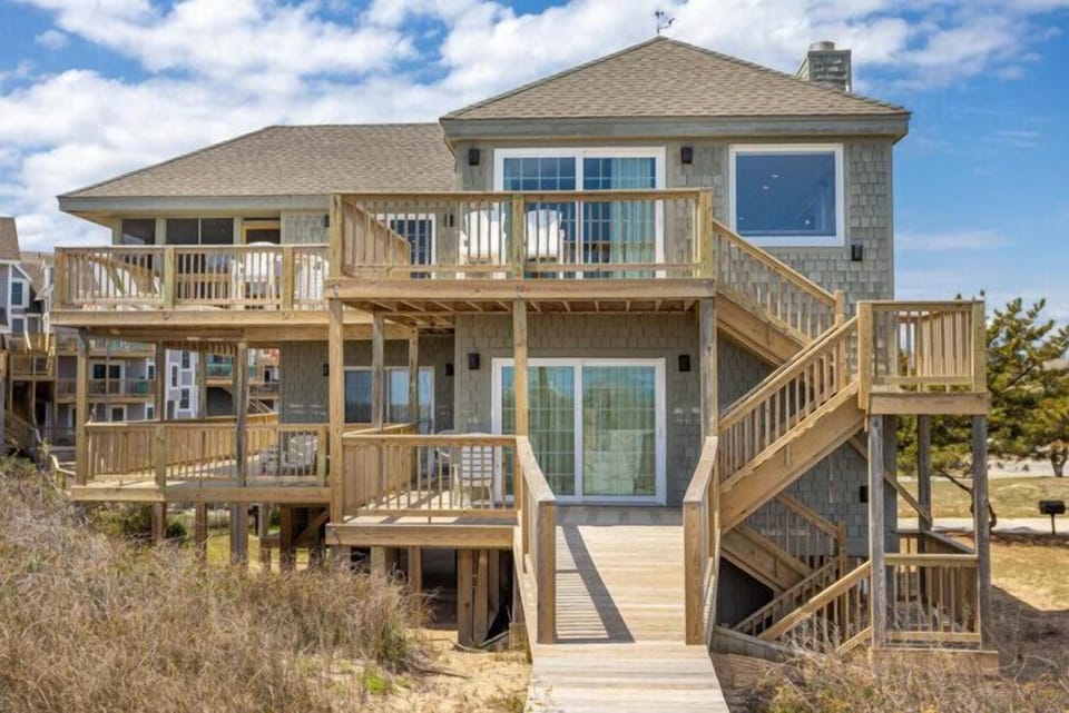 Coastal vacation home features multi-level decks and elevated design. Property provides direct beach access via wooden walkway through natural dune vegetation. Architectural style characteristic of beachfront areas.