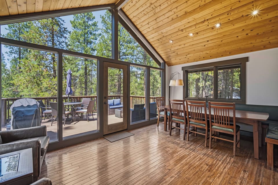 Step into your sun-drenched retreat where soaring pine ceilings and floor-to-ceiling windows frame a private forest escape. Gather around the dining table or unwind in the living area—your peaceful terrace awaits just beyond the glass doors.