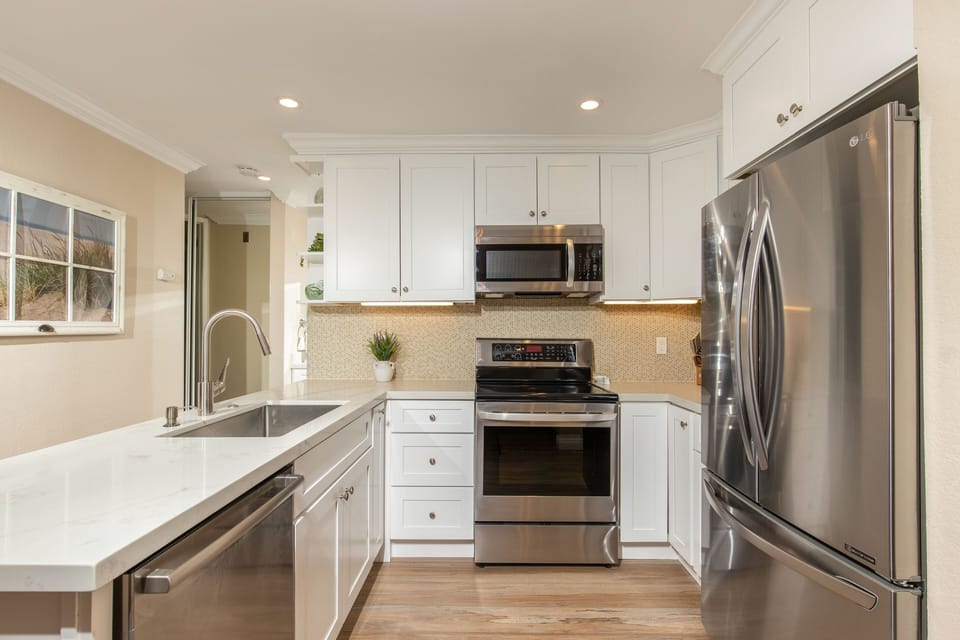 The chef's kitchen has a glass tile backsplash, new cabinets, electric kettle, and stainless appliances and sink.