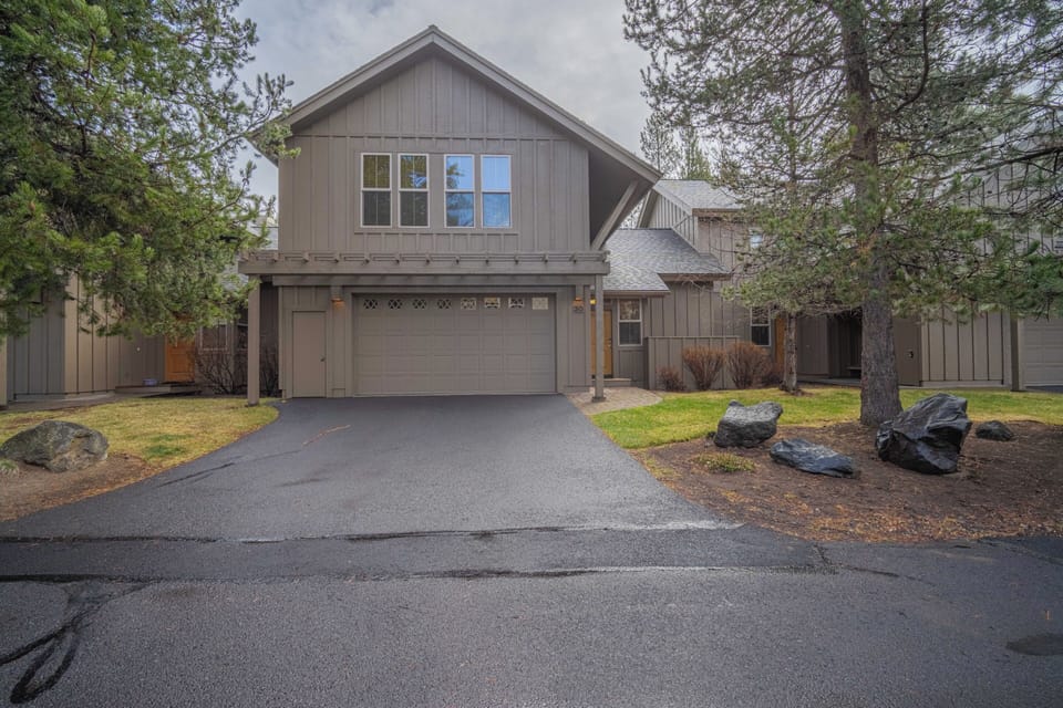 Modern two-story vacation home with attached garage, surrounded by mature trees and natural landscaping in a quiet residential setting.