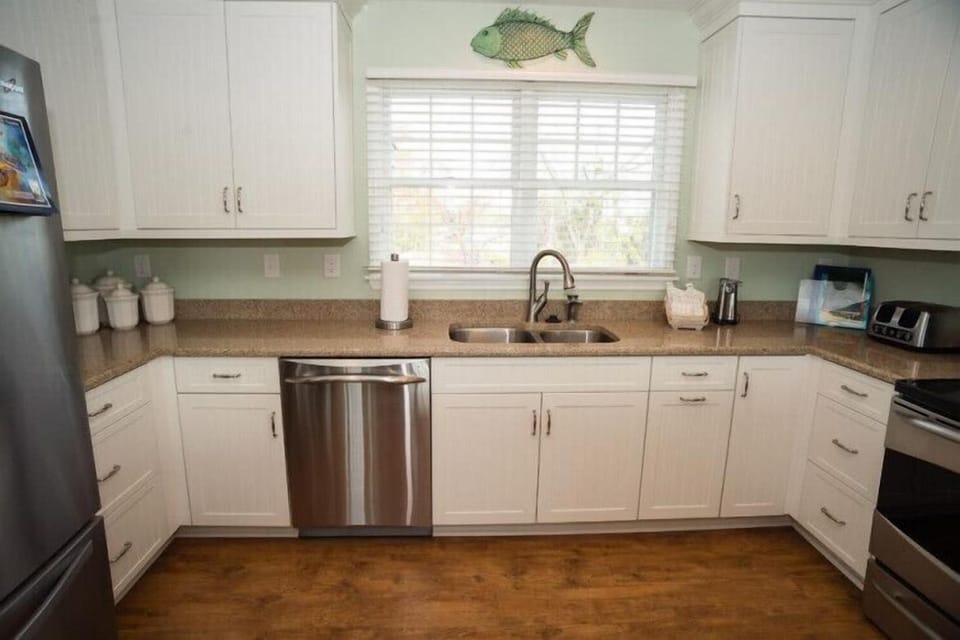 Your fully equipped kitchen invites you to prepare meals with ease, featuring stainless appliances, ample counter space, and coastal charm with a cheerful fish accent above the window.
