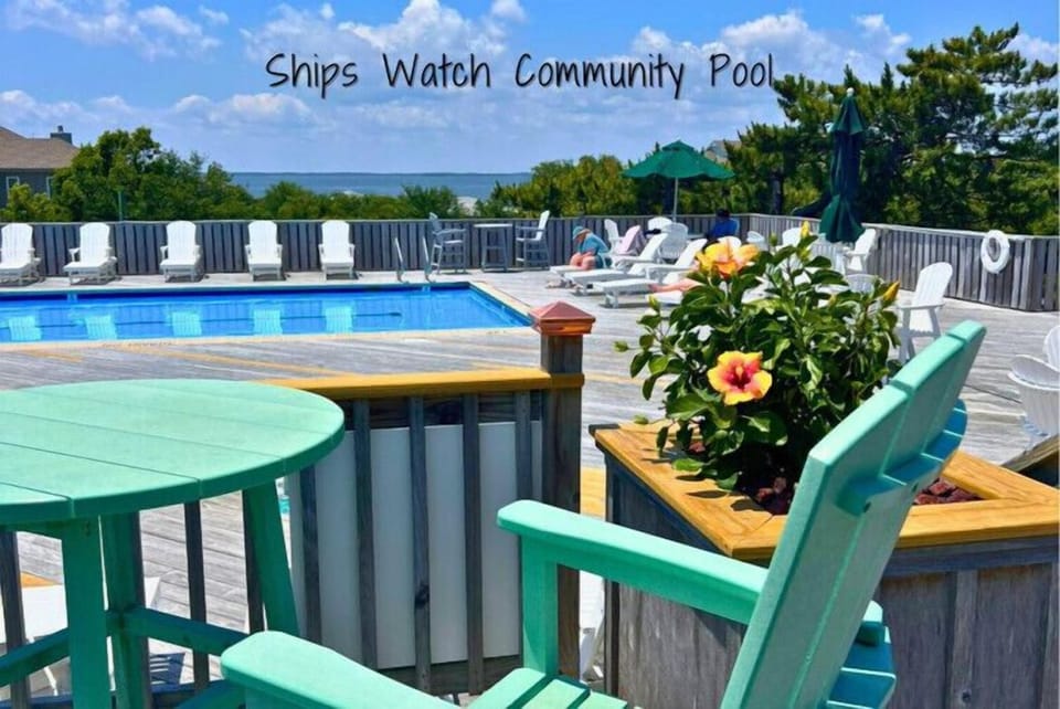 The Ships Watch Community Pool offers a serene outdoor escape with sparkling blue waters, plenty of lounge chairs, and vibrant flowers—perfect for relaxing under the sun or enjoying a refreshing swim.