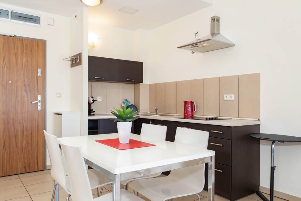 A dining area with a sleek white table and chairs for four, adjacent to a modern kitchen, creating a functional and social cooking and eating space.